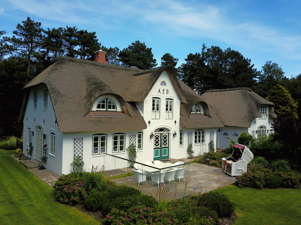 Imagen de fachada de casa blanca campestre grande de tres plantas con revestimiento de ladrillo y tejado a cuatro aguas