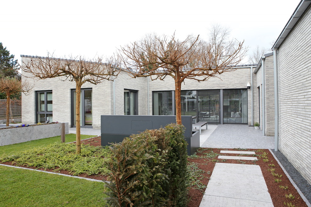 Large and gey contemporary bungalow detached house in Munich with stone cladding, a lean-to roof and a tiled roof.