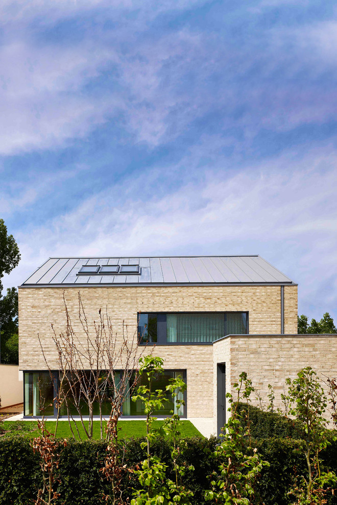 Esempio della villa beige moderna a due piani di medie dimensioni con rivestimento in mattoni, tetto a capanna e copertura in metallo o lamiera