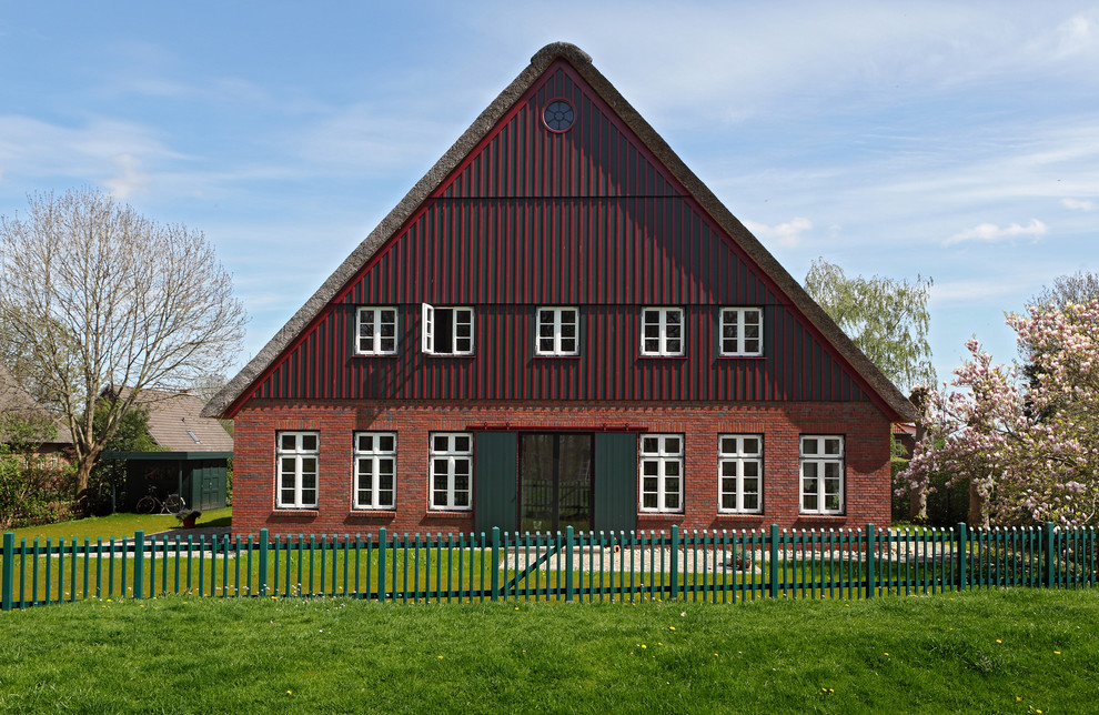 Immagine della facciata di una casa ampia rossa country a tre piani con rivestimento in mattoni e tetto a capanna