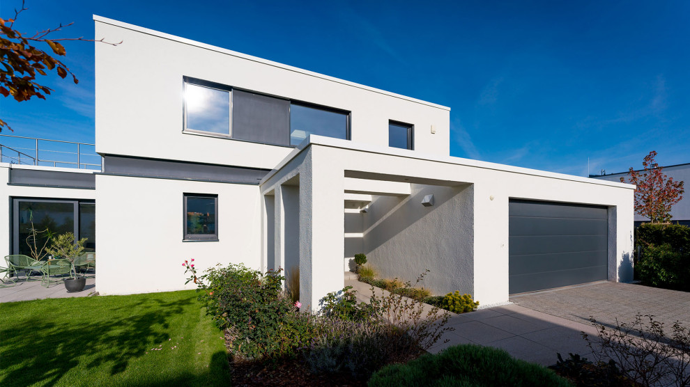 Стильный дизайн: двухэтажный, белый частный загородный дом среднего размера в современном стиле с облицовкой из цементной штукатурки и плоской крышей - последний тренд