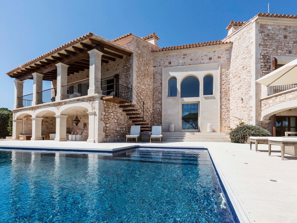 Idées déco pour une grande façade de maison beige méditerranéenne en pierre à un étage avec un toit plat et un toit en tuile.