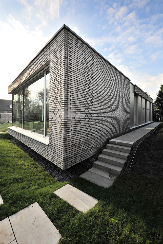 Esempio della villa ampia grigia contemporanea a un piano con rivestimento in mattoni e tetto piano