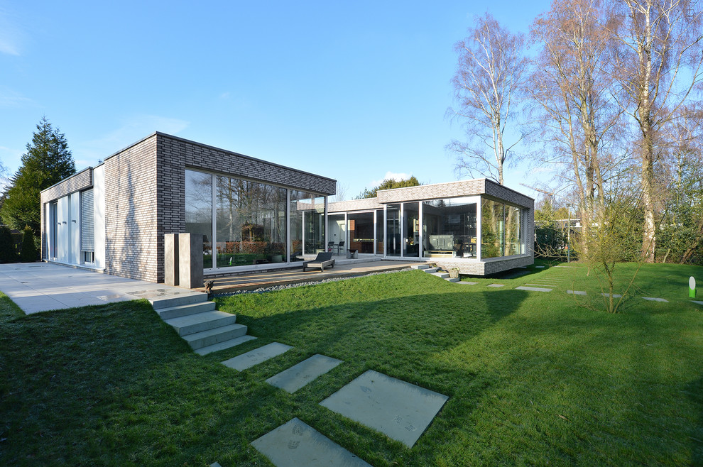 Exempel på ett mycket stort modernt grått hus, med allt i ett plan, tegel och platt tak