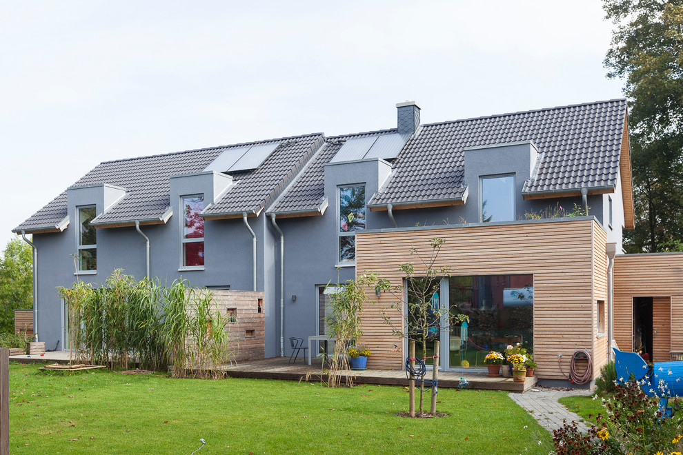 Modelo de fachada de casa bifamiliar gris actual grande de dos plantas con revestimiento de estuco, tejado plano y tejado de teja de barro