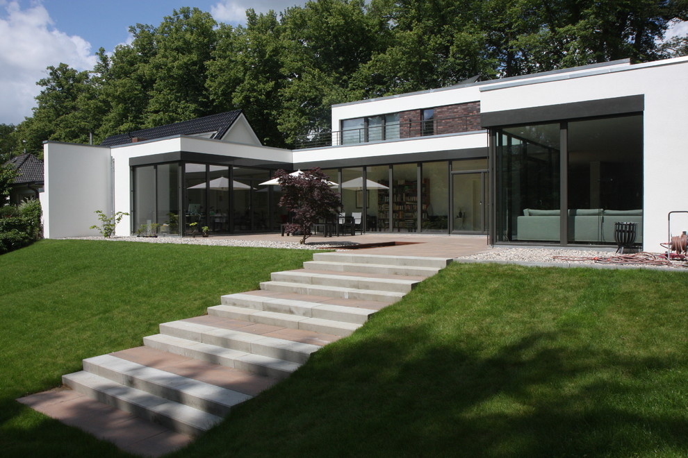 Modelo de fachada de casa blanca actual de tamaño medio de dos plantas con revestimientos combinados, tejado plano y techo verde