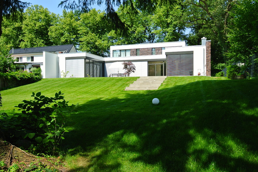Cette photo montre une très grande façade de maison blanche tendance en pierre de plain-pied avec un toit plat et un toit végétal.