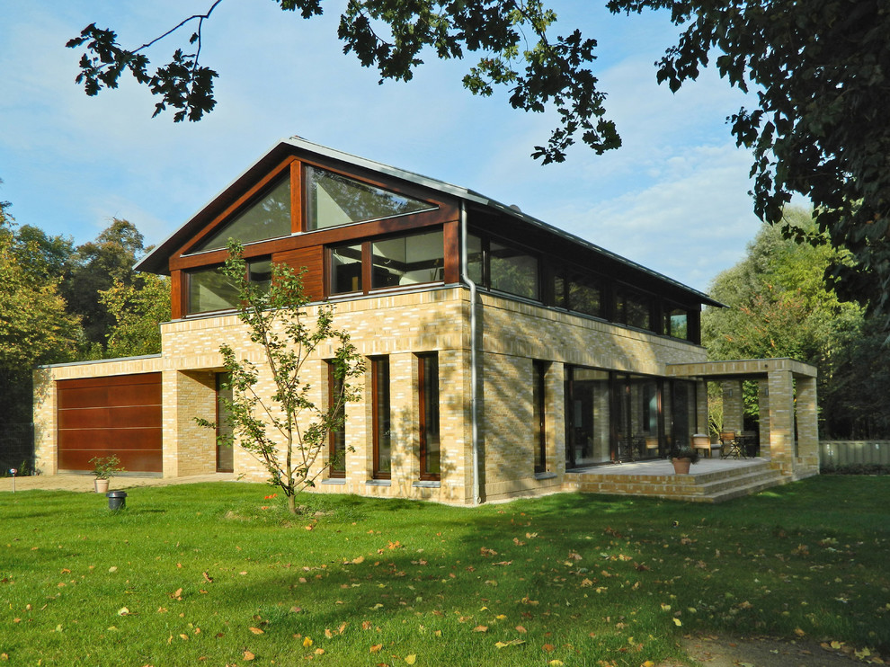 Стильный дизайн: двухэтажный, бежевый дом среднего размера в современном стиле с комбинированной облицовкой и двускатной крышей - последний тренд