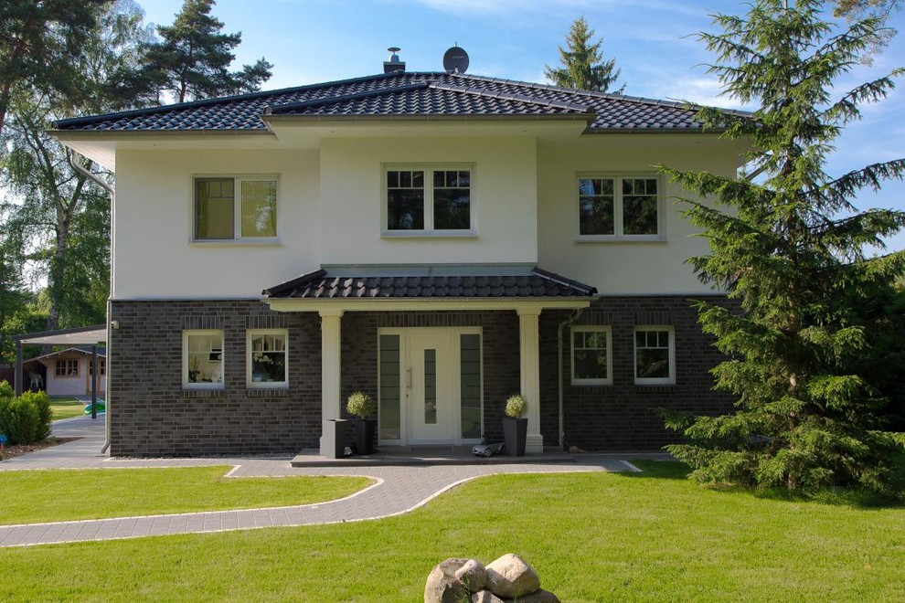 На фото: двухэтажный, разноцветный дом среднего размера в стиле неоклассика (современная классика) с комбинированной облицовкой, вальмовой крышей и крышей из гибкой черепицы