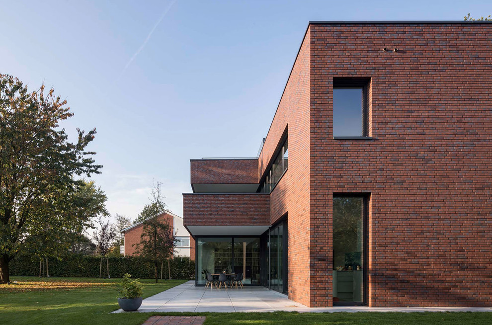 Imagen de fachada de casa roja minimalista grande de dos plantas con revestimiento de ladrillo y tejado plano