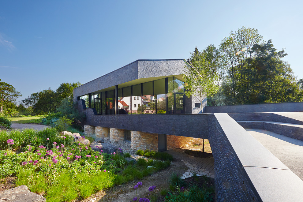 Свежая идея для дизайна: двухэтажный, серый частный загородный дом в современном стиле с облицовкой из камня и двускатной крышей - отличное фото интерьера