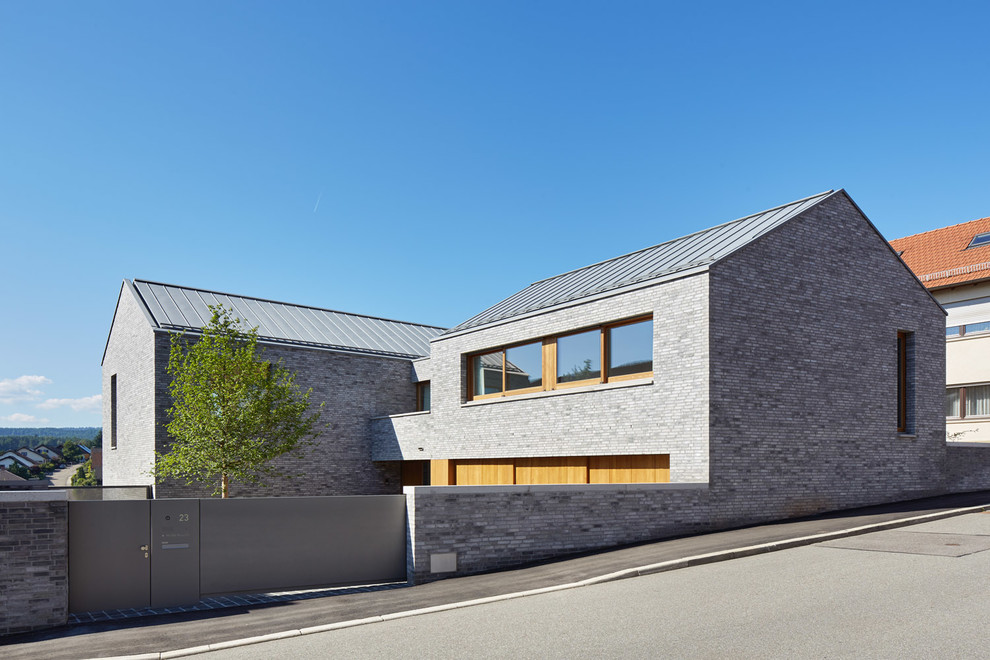 Modelo de fachada de casa gris moderna grande de dos plantas con revestimiento de ladrillo, tejado a dos aguas y tejado de metal