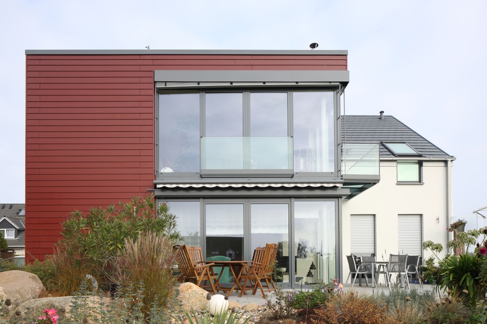 Imagen de fachada de casa roja actual de tamaño medio de dos plantas con revestimiento de aglomerado de cemento y tejado plano