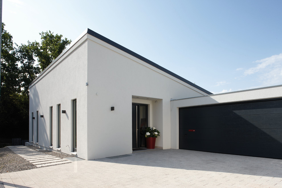 Стильный дизайн: одноэтажный, белый дом среднего размера в современном стиле с односкатной крышей и облицовкой из цементной штукатурки - последний тренд