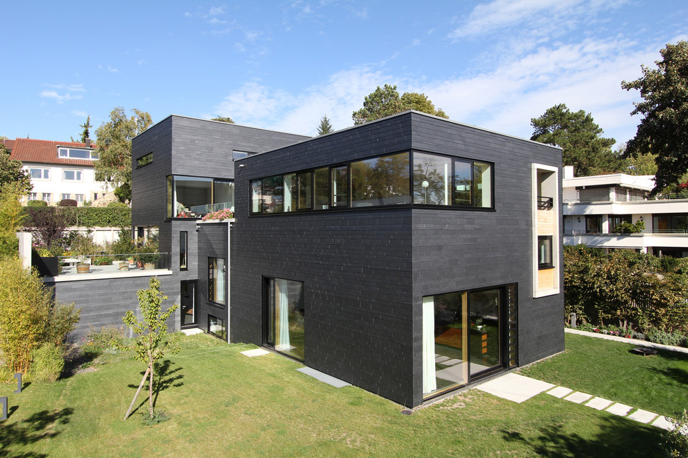 Cette image montre une grande façade de maison grise design en pierre à niveaux décalés avec un toit plat.