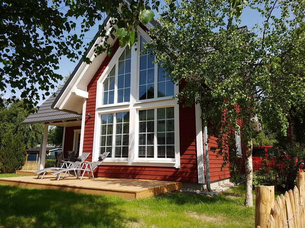 Esempio della villa piccola rossa scandinava a un piano con rivestimento in legno, tetto a capanna e copertura in tegole