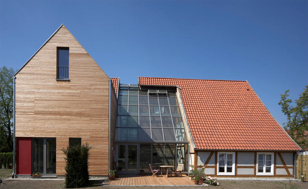 This is an example of a medium sized rural two floor house exterior in Other with wood cladding and a tiled roof.