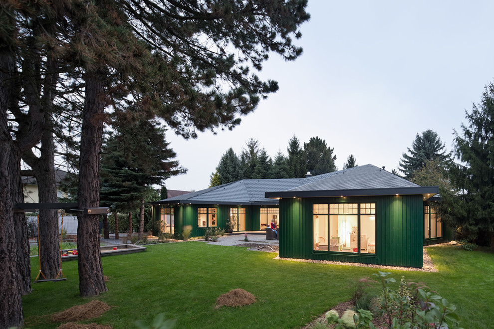 На фото: одноэтажный, зеленый, деревянный дом среднего размера в современном стиле с вальмовой крышей с
