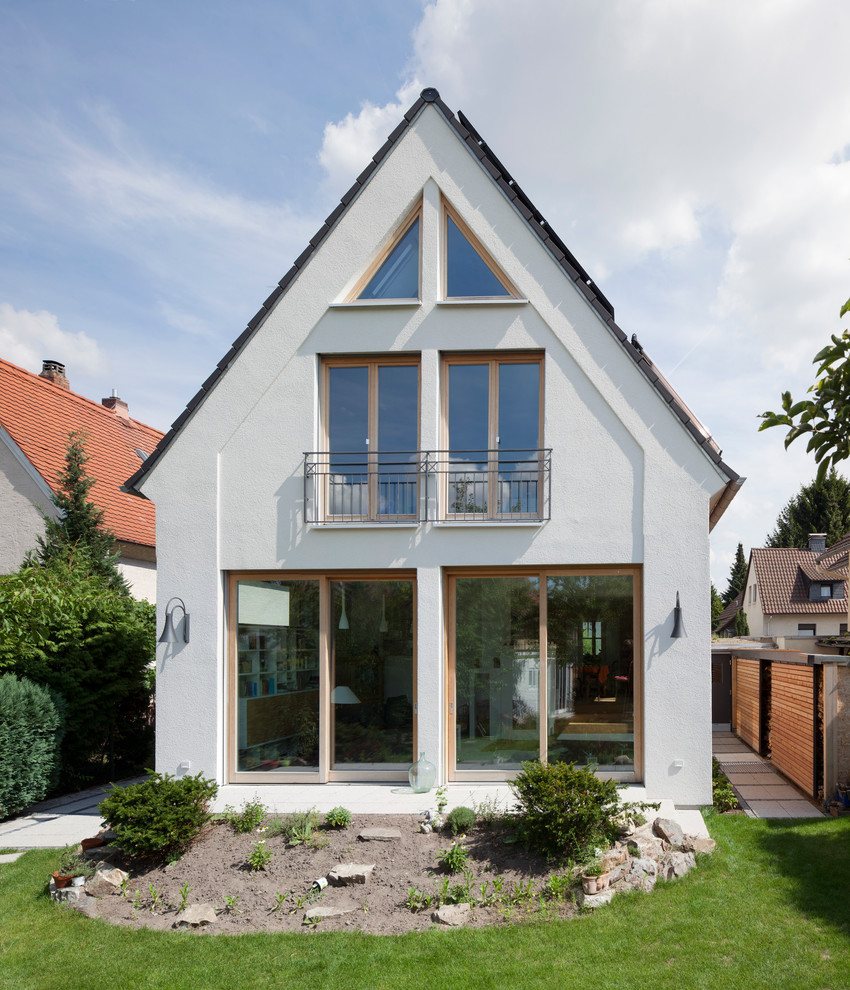 На фото: двухэтажный, белый, маленький дом в стиле неоклассика (современная классика) с облицовкой из цементной штукатурки и двускатной крышей для на участке и в саду с