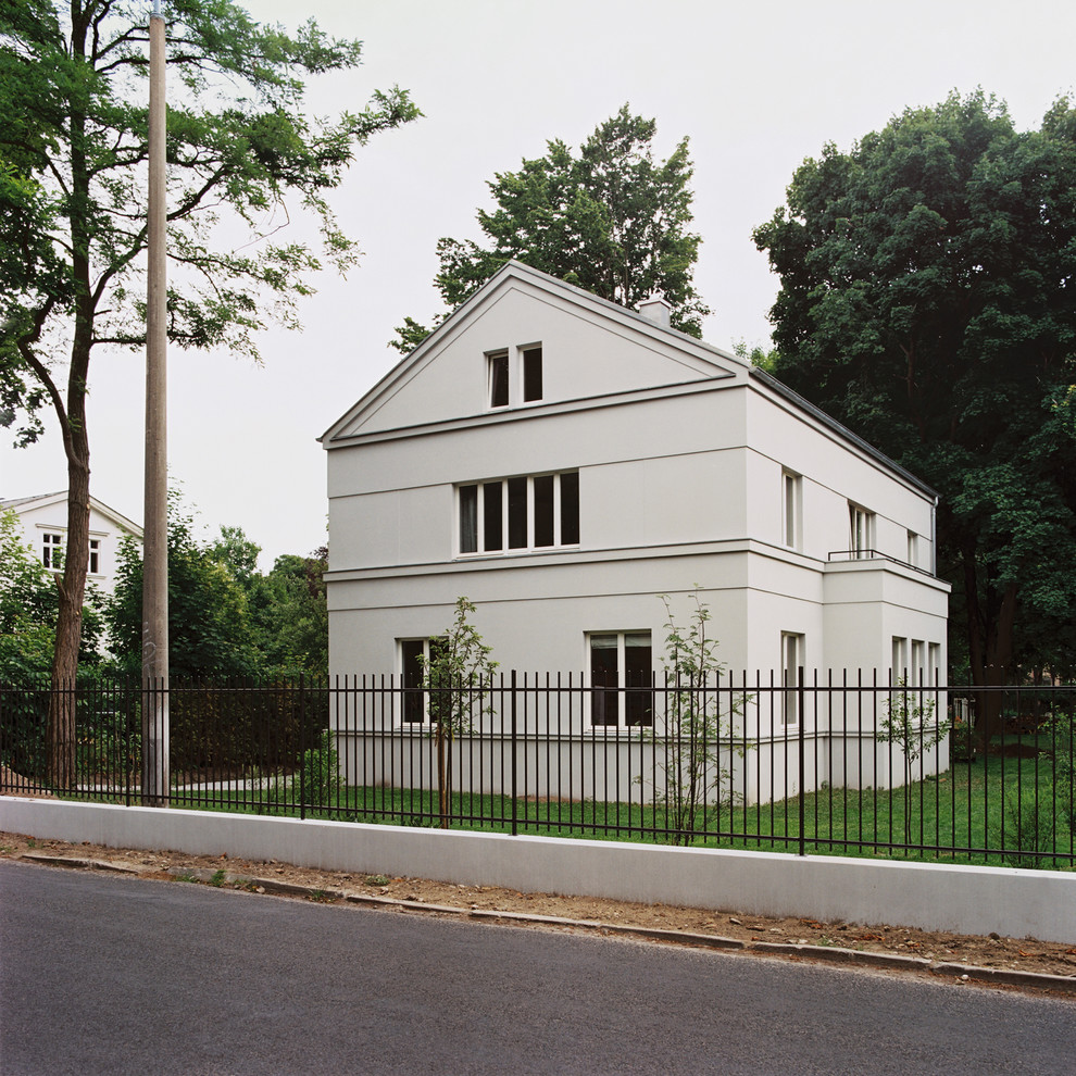 На фото: трехэтажный, бежевый дом среднего размера в стиле неоклассика (современная классика) с двускатной крышей и облицовкой из камня с