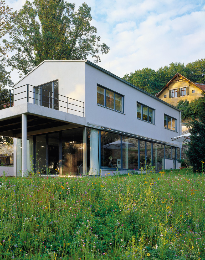 На фото: большой, двухэтажный, серый дом в современном стиле с облицовкой из цементной штукатурки и двускатной крышей