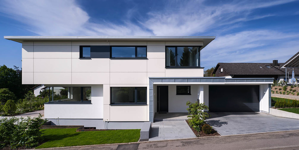 Immagine della facciata di una casa beige contemporanea a due piani di medie dimensioni con tetto piano, rivestimento con lastre in cemento e terreno in pendenza