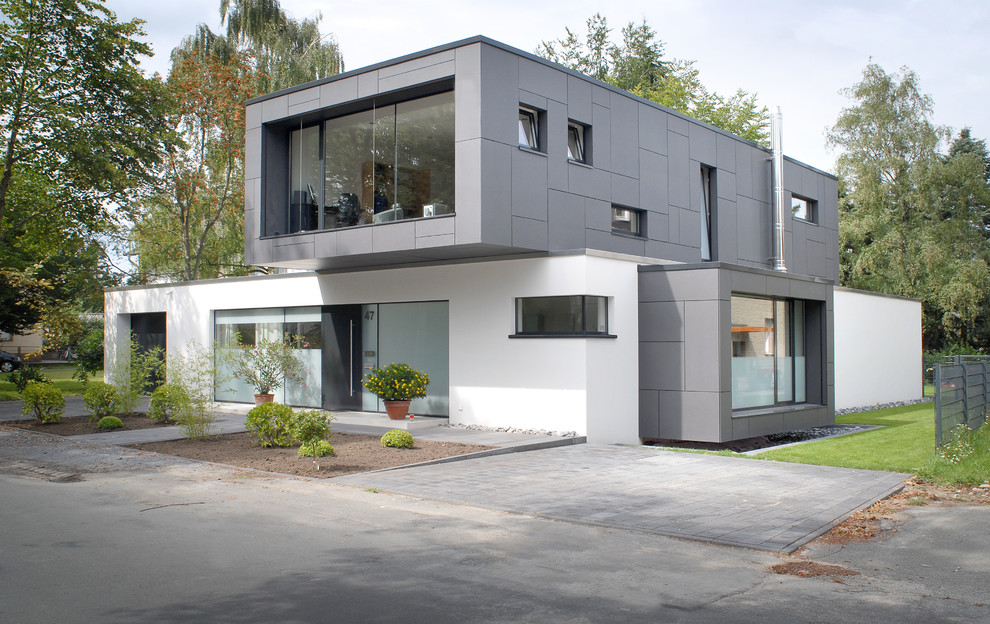 На фото: белый частный загородный дом среднего размера в стиле модернизм с разными уровнями, облицовкой из цементной штукатурки и плоской крышей