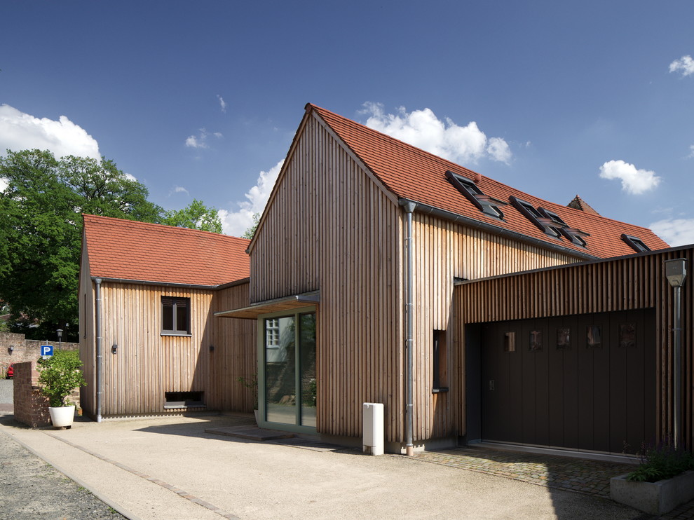 Esempio della villa marrone scandinava a due piani di medie dimensioni con rivestimento in legno e tetto a capanna