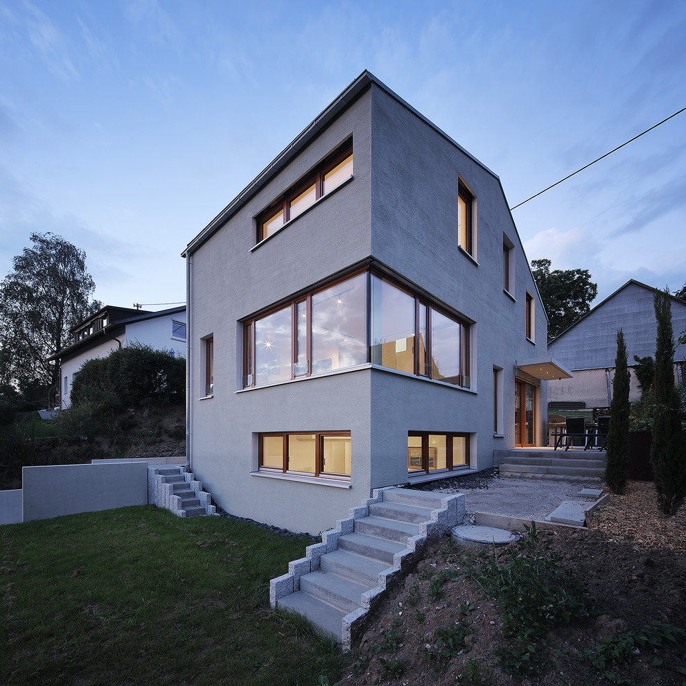 Modelo de fachada de casa gris actual grande de tres plantas con revestimiento de estuco y tejado a dos aguas
