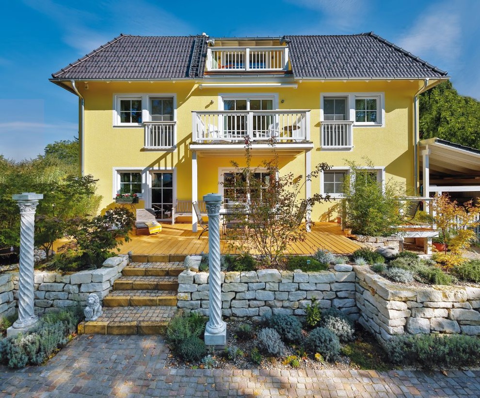 Diseño de fachada de casa amarilla clásica de tres plantas con tejado a cuatro aguas y tejado de teja de barro