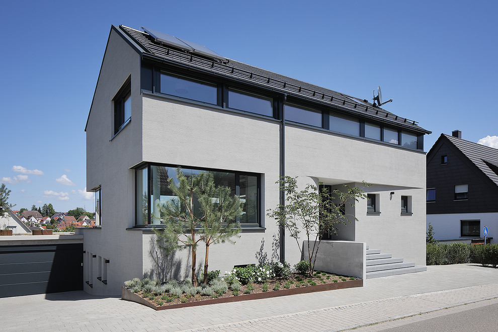 Ejemplo de fachada de casa gris actual de tamaño medio de tres plantas con revestimiento de estuco y tejado a dos aguas
