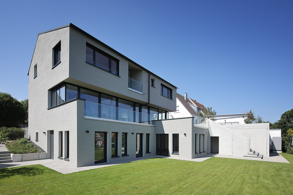 Ejemplo de fachada de casa gris actual grande de tres plantas con revestimiento de estuco y tejado a dos aguas