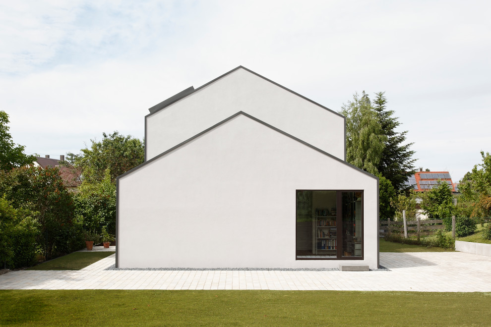 Пример оригинального дизайна: маленький, двухэтажный, белый дом в современном стиле с облицовкой из бетона и двускатной крышей для на участке и в саду