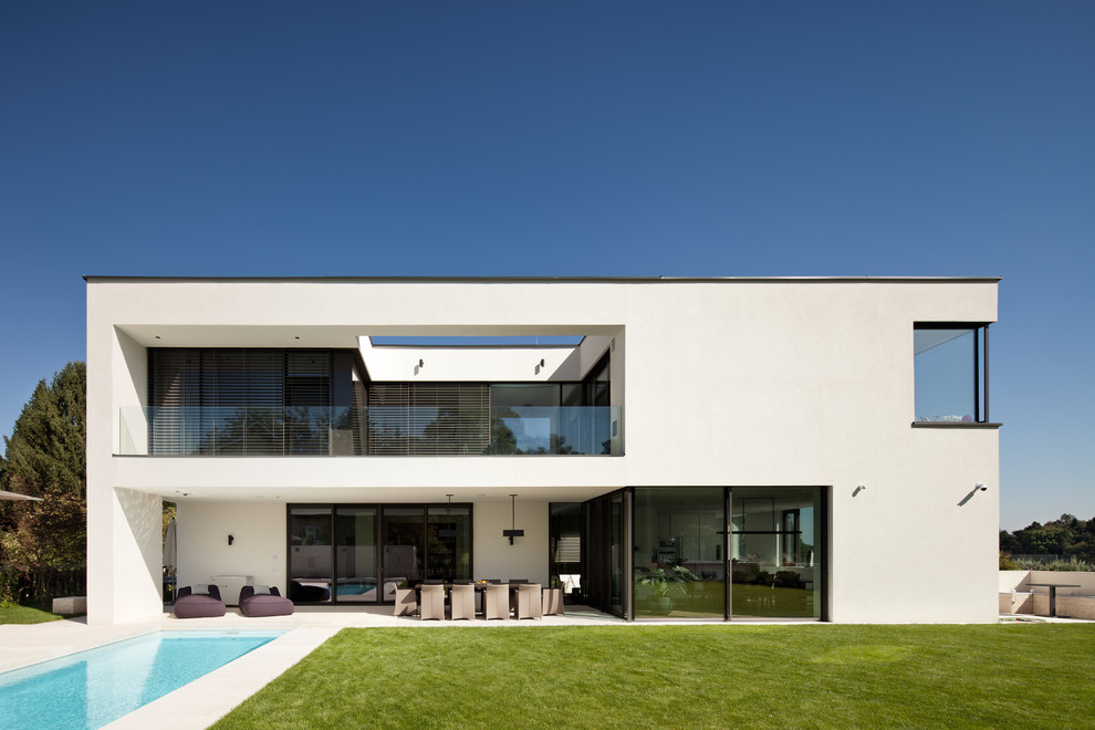 Свежая идея для дизайна: двухэтажный, белый дом в современном стиле с облицовкой из цементной штукатурки и плоской крышей - отличное фото интерьера