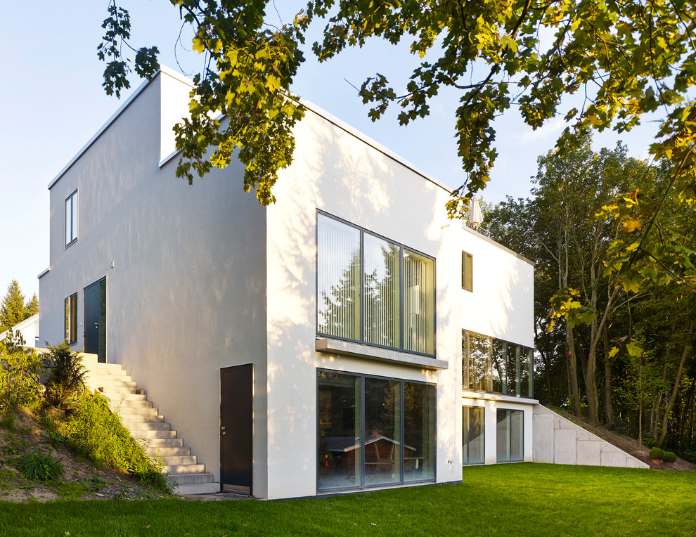 Modelo de fachada blanca contemporánea grande de tres plantas con revestimiento de estuco y tejado plano