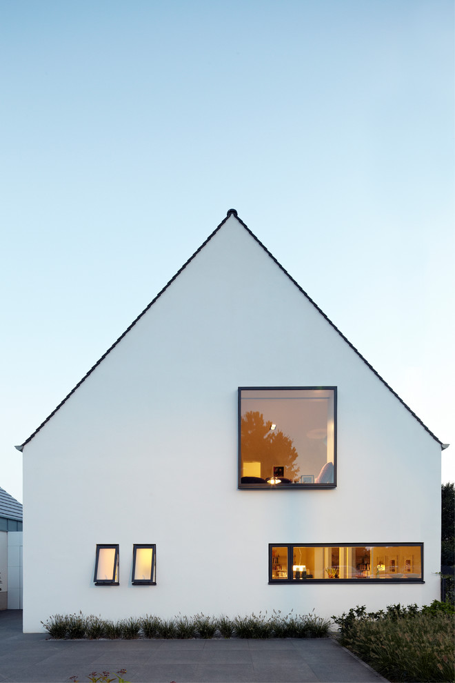 Пример оригинального дизайна: большой, белый, трехэтажный частный загородный дом в современном стиле с двускатной крышей, облицовкой из цементной штукатурки и черепичной крышей