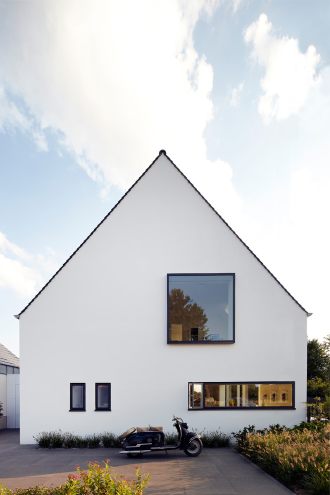 Идея дизайна: белый частный загородный дом в современном стиле с облицовкой из цементной штукатурки и двускатной крышей