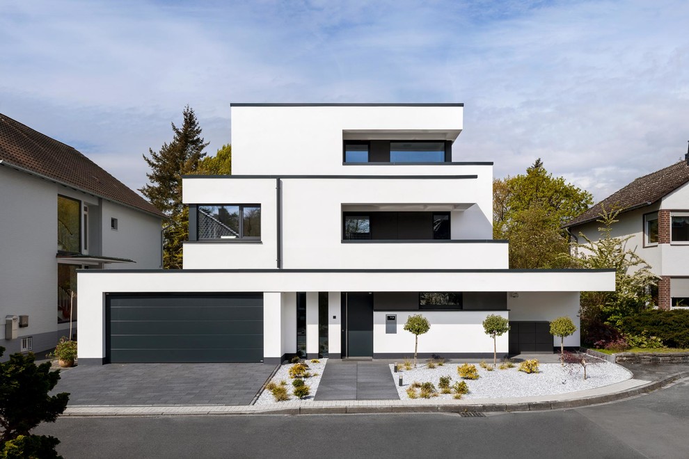 This is an example of a white and large contemporary concrete house exterior in Cologne with three floors and a flat roof.