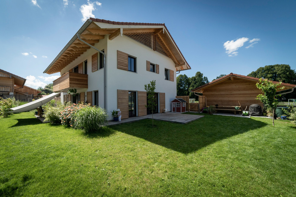 This is an example of a large and beige rural two floor render detached house in Munich with a pitched roof, a tiled roof, a grey roof and board and batten cladding.