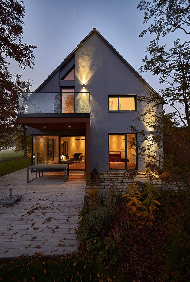 На фото: серый, большой, двухэтажный частный загородный дом в современном стиле с облицовкой из цементной штукатурки, двускатной крышей и черепичной крышей