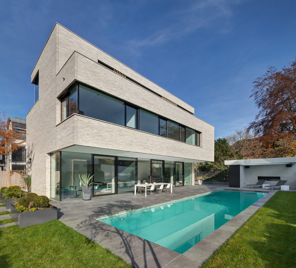Cette image montre une grande façade de maison beige minimaliste à deux étages et plus avec un toit plat.