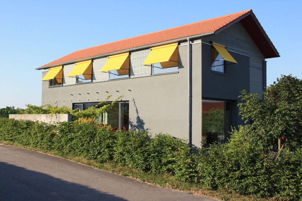На фото: серый, двухэтажный дом среднего размера в современном стиле с комбинированной облицовкой и двускатной крышей