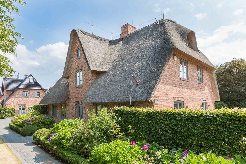 Großes, Dreistöckiges Landhausstil Einfamilienhaus mit Backsteinfassade, roter Fassadenfarbe und Walmdach in Sonstige