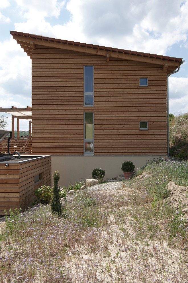 Cette image montre une façade de maison beige design en bois et bardage à clin de taille moyenne et à deux étages et plus avec un toit en appentis et un toit en tuile.