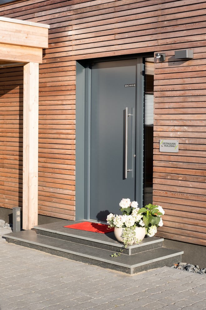 This is an example of an expansive modern bungalow front house exterior in Essen with wood cladding, a flat roof and shiplap cladding.