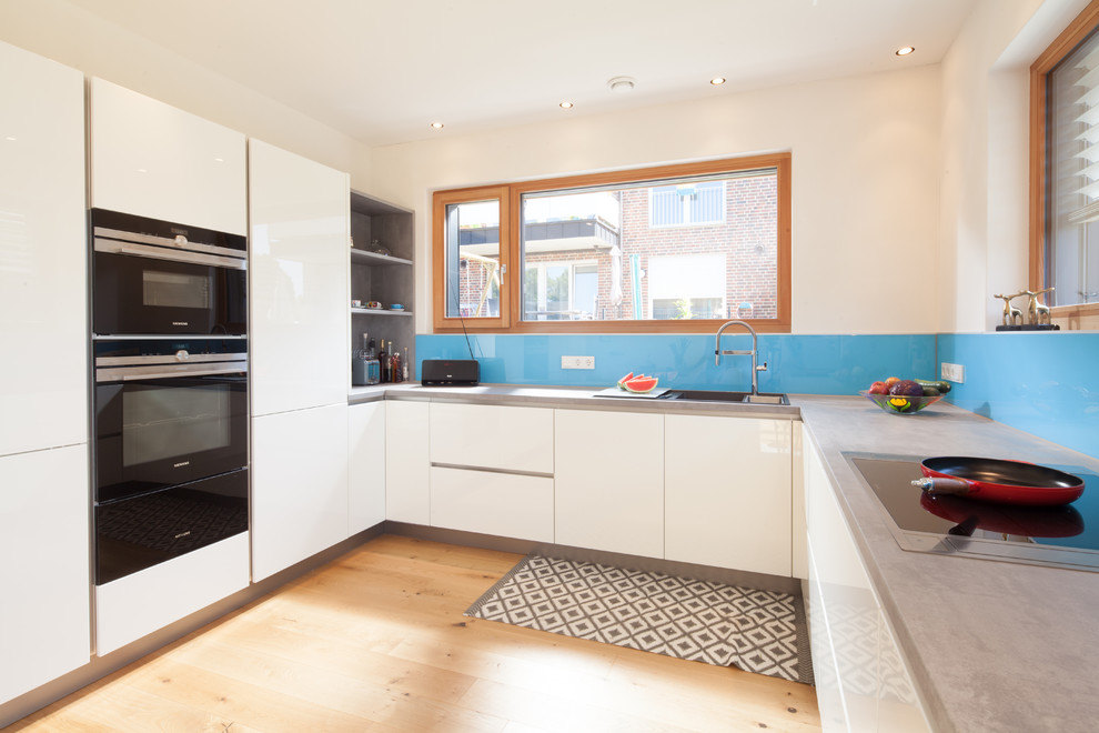 Foto di un'ampia cucina minimalista con ante lisce, ante bianche, top in cemento, paraspruzzi blu, parquet chiaro e top grigio