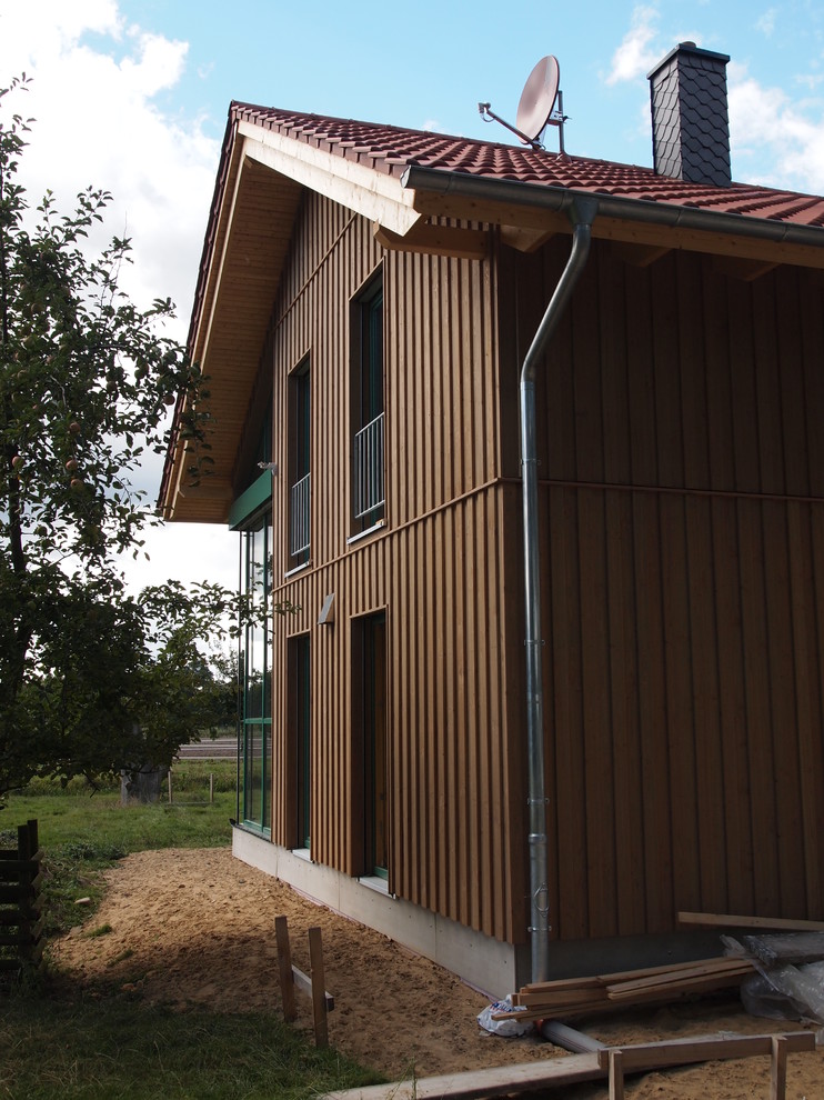 Cette photo montre une façade de maison marron tendance en bois de taille moyenne et à un étage avec un toit à deux pans et un toit en tuile.