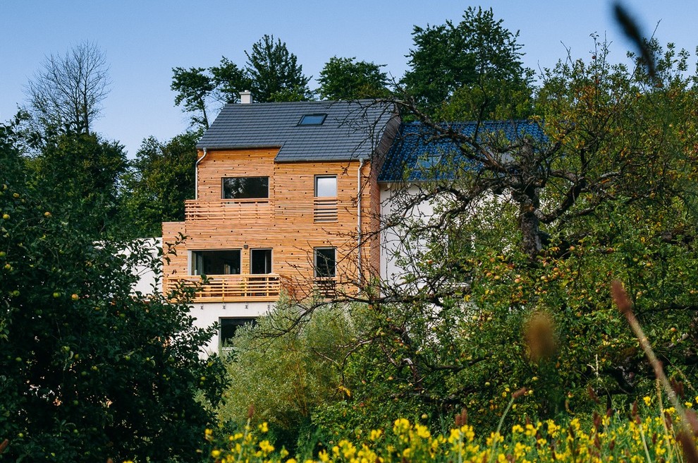 Cette image montre une très grande façade de maison beige design en bois à niveaux décalés avec un toit à deux pans, un toit en tuile et un toit noir.