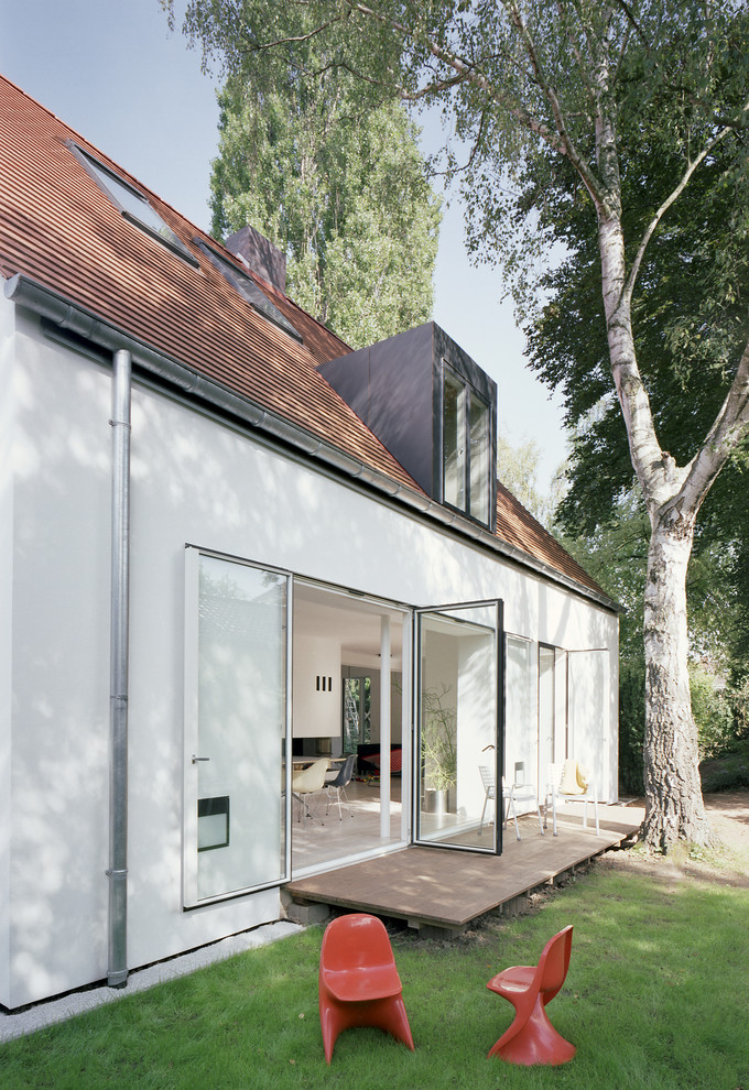 На фото: двухэтажный, белый частный загородный дом среднего размера в современном стиле с двускатной крышей и облицовкой из цементной штукатурки с