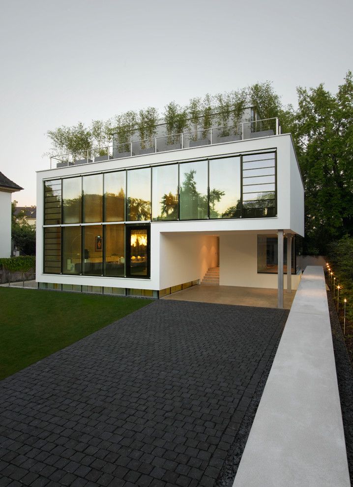 Réalisation d'une grande façade de maison blanche design en verre à un étage avec un toit plat.
